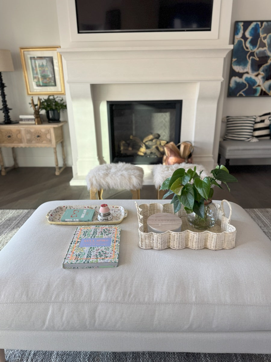 White scalloped wicker basket sitting on an ottoman acting as a display piece