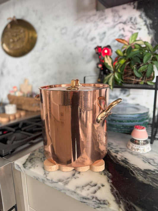 copper pot sitting on a scalloped oak trivet