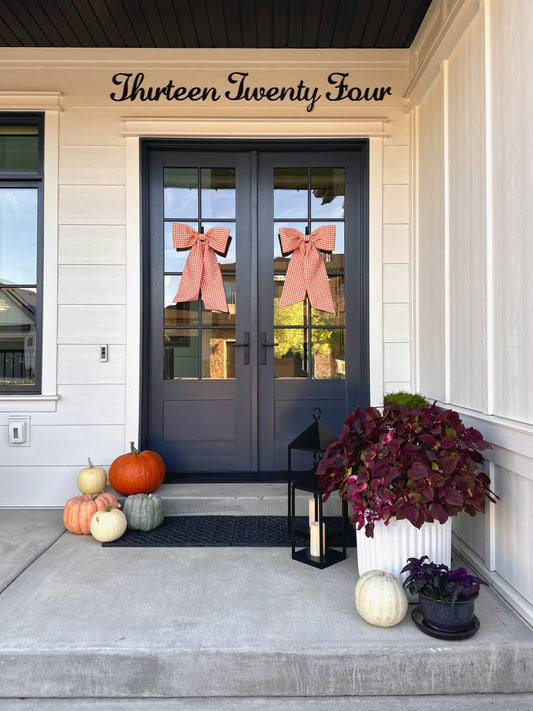 Front doors styled with matching orange gingham bows, surrounded by stacked pumpkins, a lantern, and fall plants
