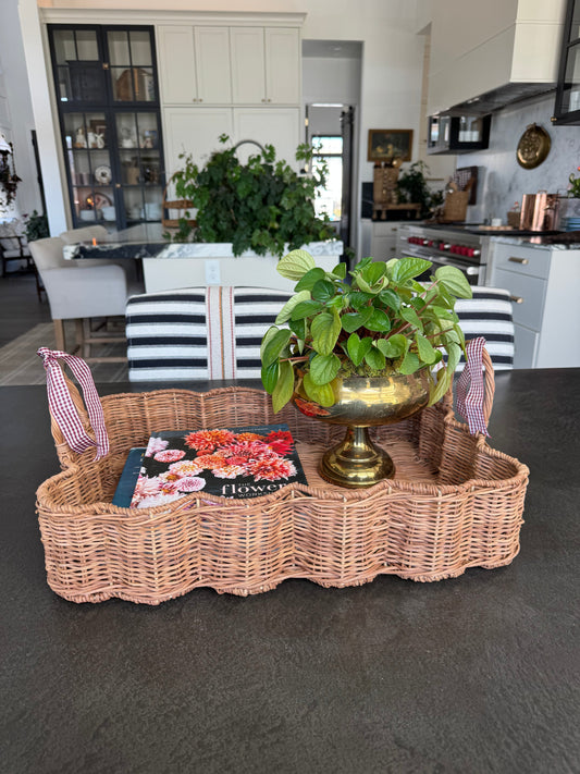Scalloped wicker basket with a book and a pot of green foliage set on a kitchen table.