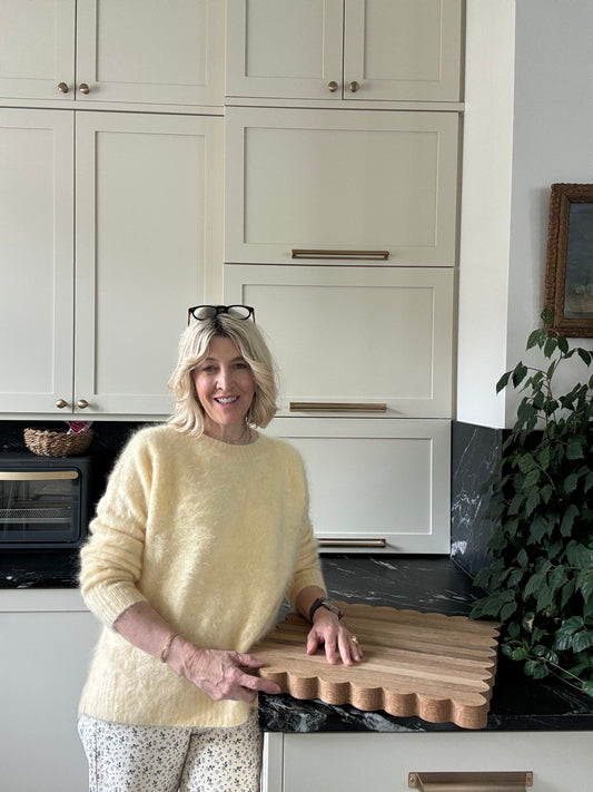 Jeniel standing with her elbow and hand propped on oak cutting board