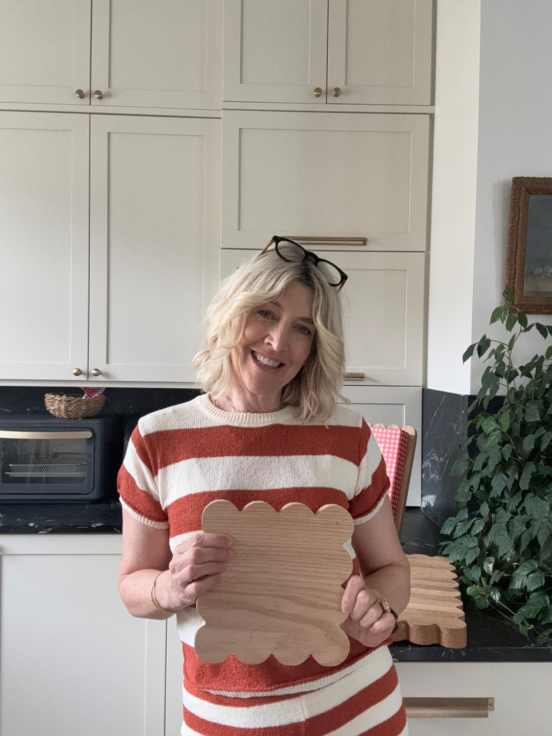 Jeneil stands in her kitchen holding a scalloped oak trivet