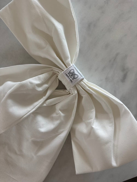 A white linen decorative bow with the logo of A Bow or Two attatched to the back
