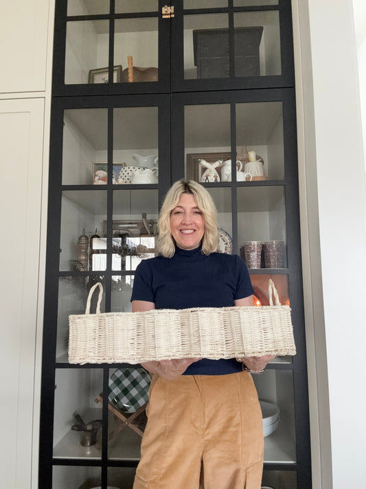Jeneil stands in front of a navy blue and glass cabinet holding a scalloped wicker basket