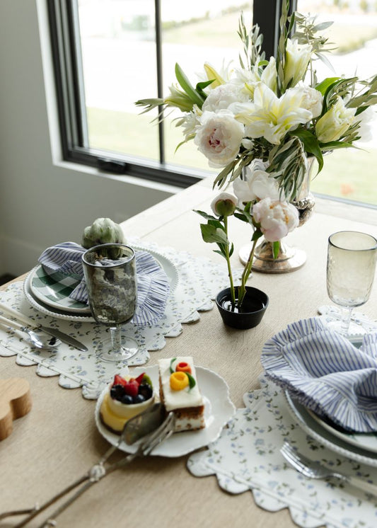 Table with white floral ruffled placemats, striped ruffled napkins, and a vase of white flowers