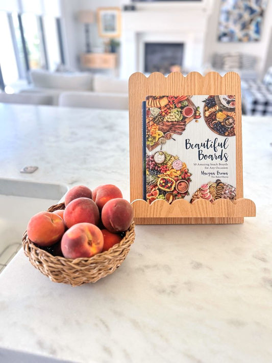 Wooden cookbook stand on white counter by bowl of peaches