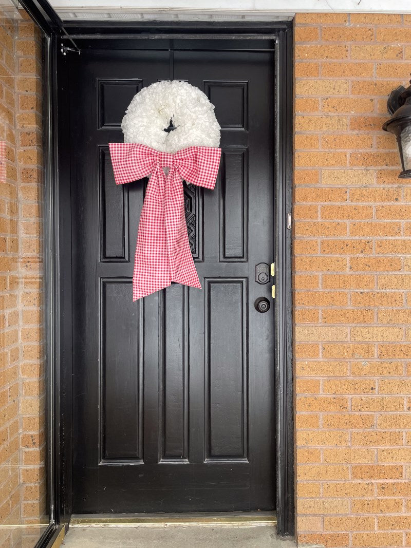 Red gingham bow with white circular wreath on a black door