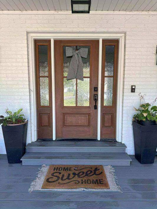 Black door bow on door with potted plants and a welcome mat