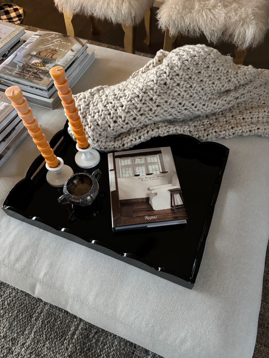 Elegant scalloped lacquer tray on an ottoman styled with candles, an open book, and a soft blanket for warm home decor inspiration
