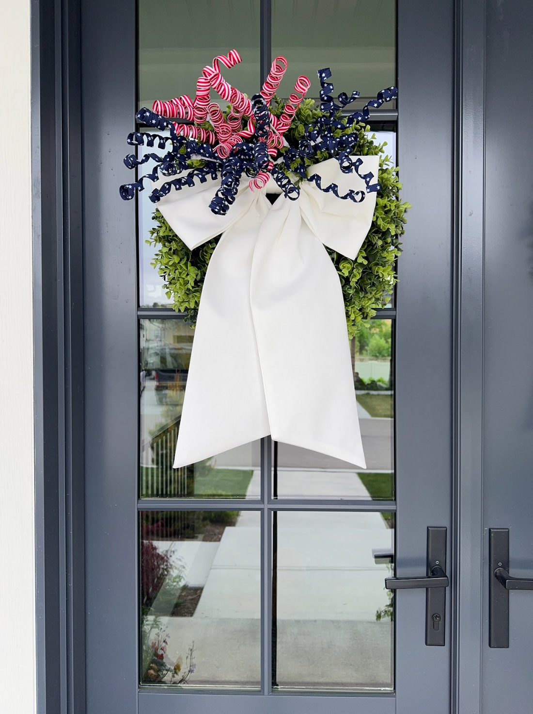 Cream gingham bow with decorative blue and pink ribbon added hanging from wreath, hanging on front door
