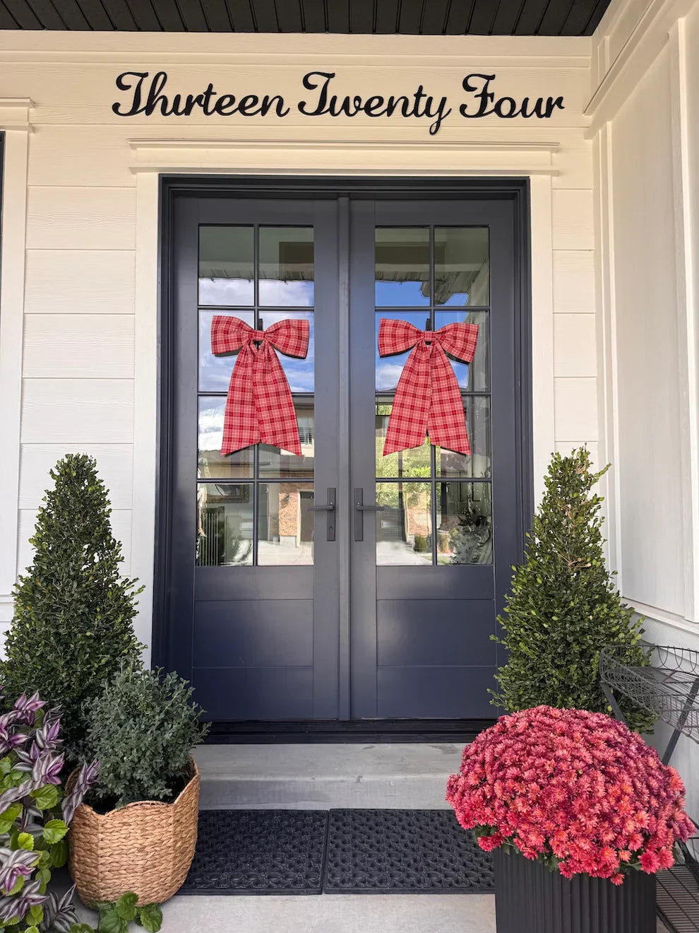 Christmas plaid bows on double doors with decorated Christmas trees and festive flowers on a holiday porch