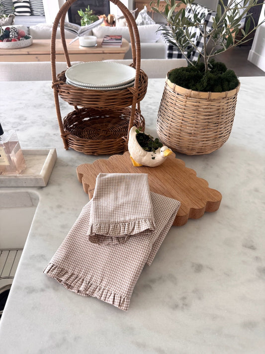 Cream gingham dish towel set layered on top of oak trivet sitting on granite countertop 