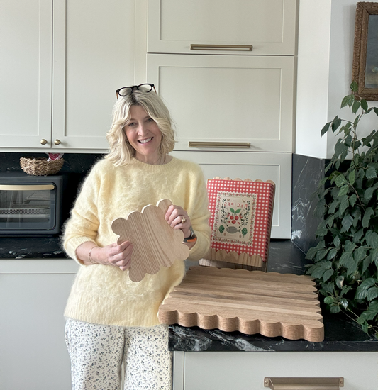 Jeneil stands with a scalloped oak cutting board, oak trivet, and cookbook stand