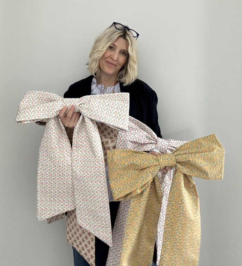 Women holding a variety of large front door decor bows in front of white wall