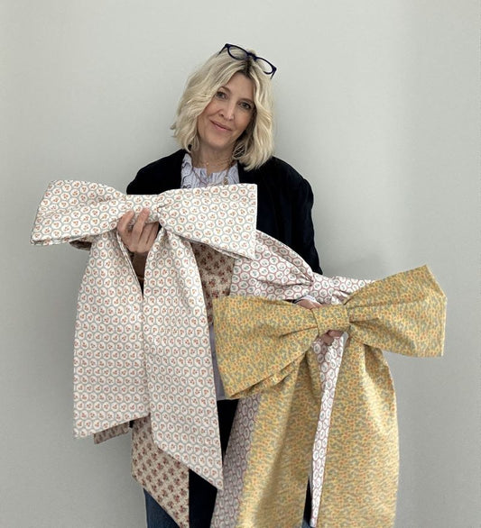 Women holding a variety of large front door decor bows in front of white wall