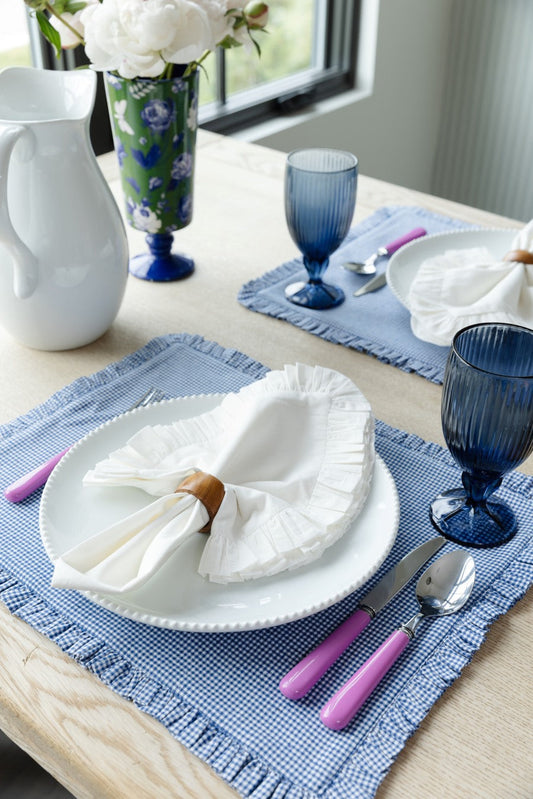 A white ruffled napkin sits on a white plate, which in turn rests on a blue ruffled placemat